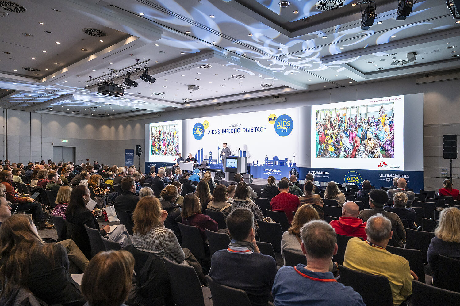 Foto vom Plenum der 20. Münchner AIDS- und Infektiologie-Tagen 2026 in Berlin. Voller Raum. Vortrag auf der Bühne.